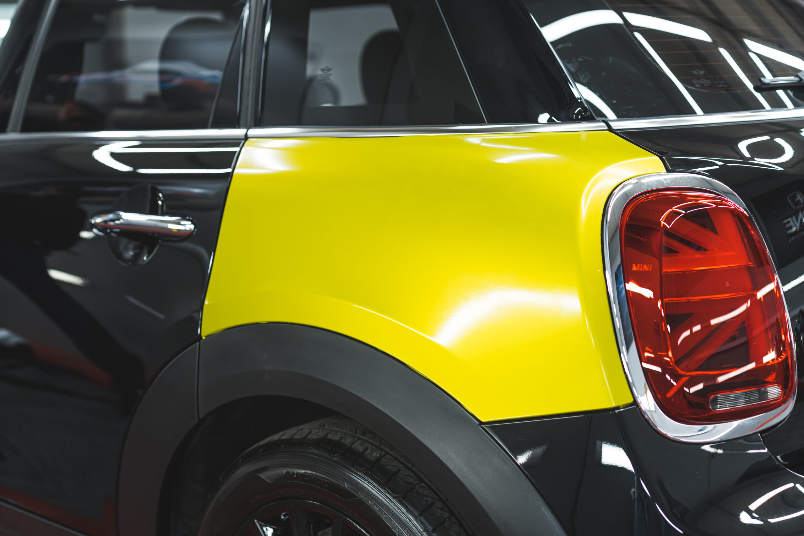 closeup shot of a neon yellow vinyl foil on a black car, car workshop. High quality photo